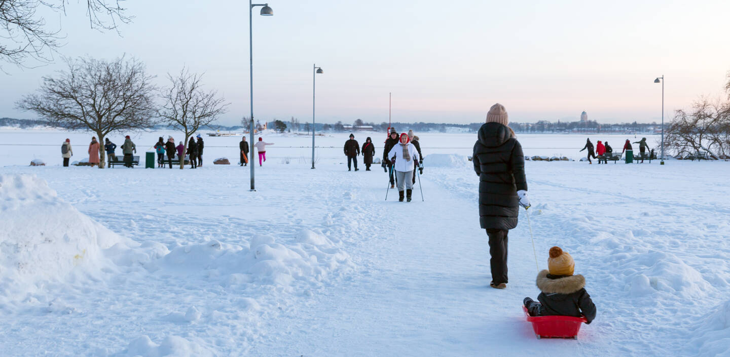 Ihmisiä lumisena talvipäivänä meren rannalla.