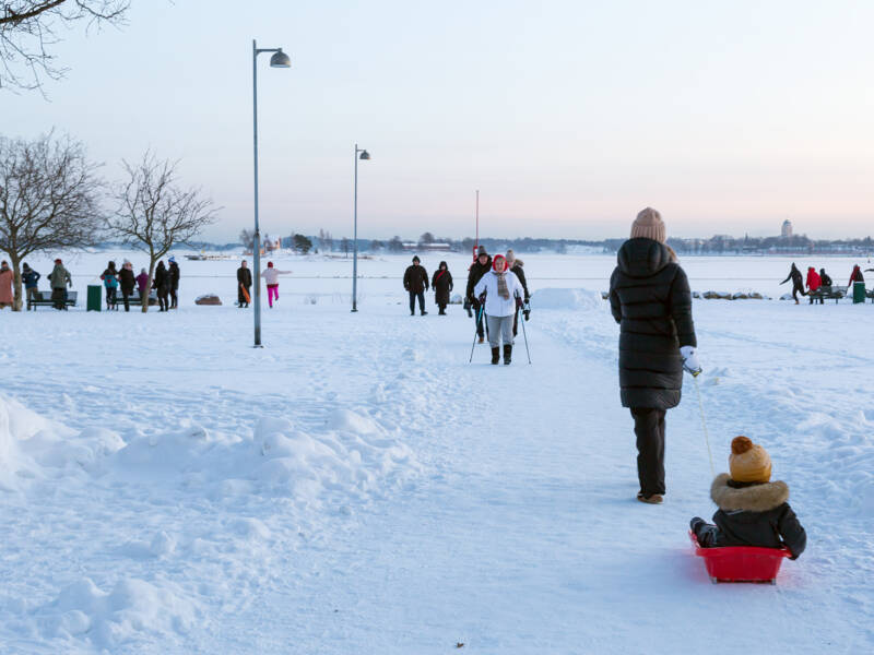 Ihmisiä lumisena talvipäivänä meren rannalla.