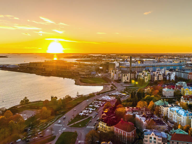 Ilmakuva Helsingin Eirasta Hernesaareen päin. Aurinko laskee meren horisonttiin.