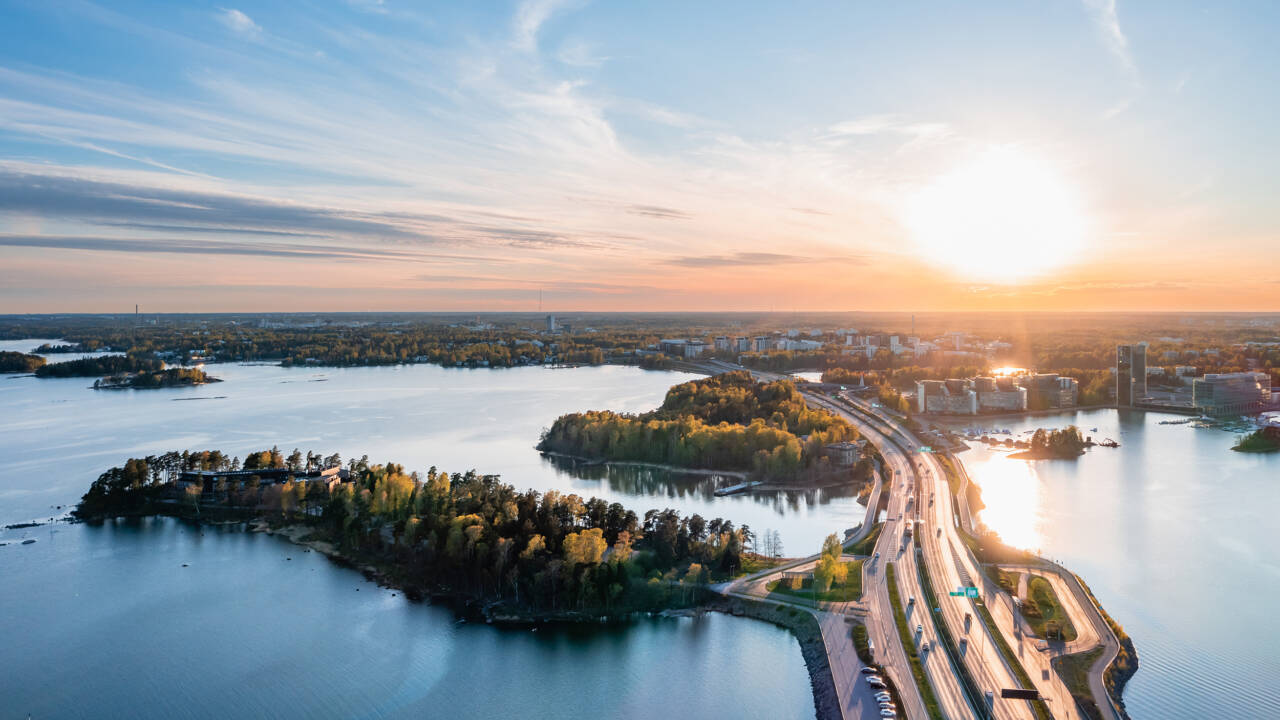 Ilmakuva Länsiväylältä Espooseen päin. Merta, autotie, puita ja kauempana kerrostaloja.