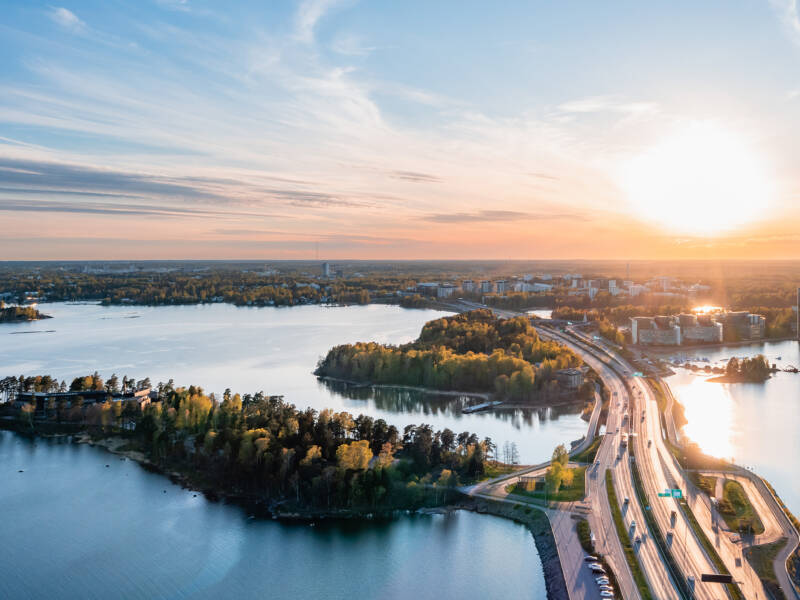 Ilmakuva Länsiväylältä Espooseen päin. Merta, autotie, puita ja kauempana kerrostaloja.