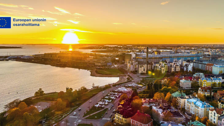 Kaupunkimaisemaa auringonlaskussa. EU-lippulogo, Euroopan unionin osarahoittama.