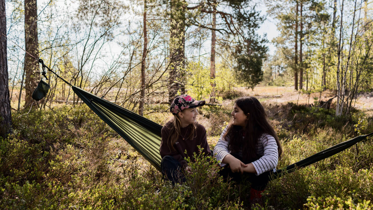 Kaksi tyttöä istumassa riippukeinussa metsässä